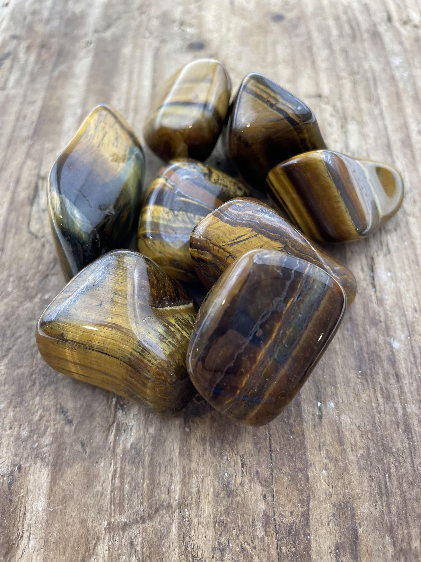 Tigerøje sten samlet i en klynge på en træoverflade, med deres karakteristiske gyldne og brune striber.