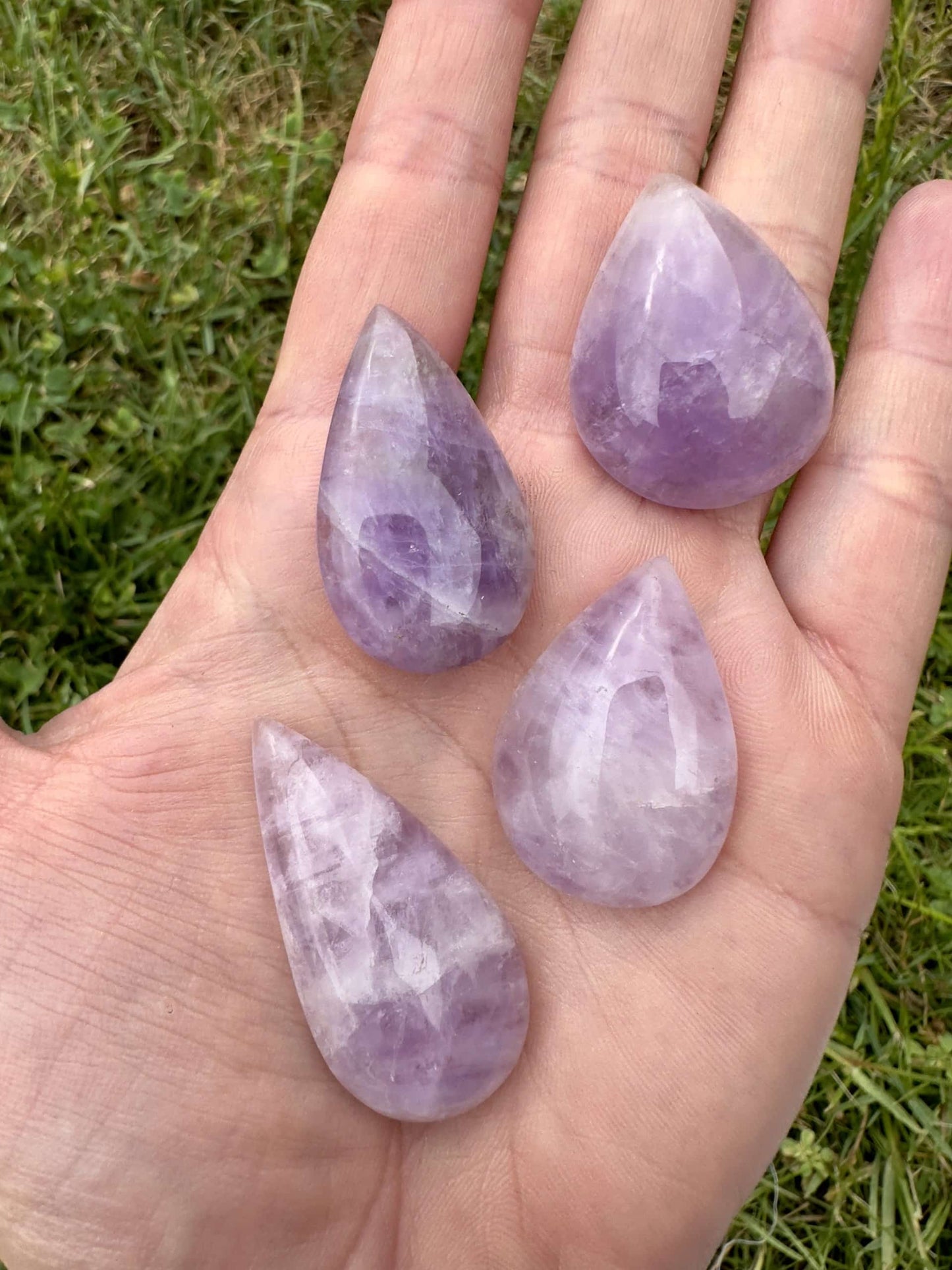 Hånd med fire ametyst dråber mod en baggrund af græs.