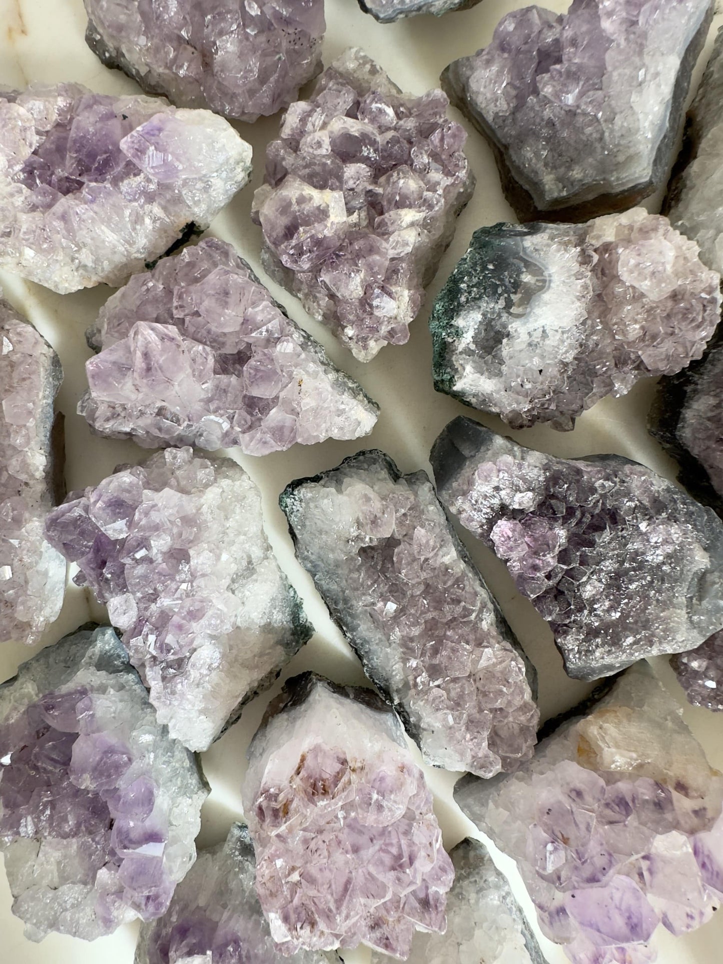 Ametyst klynger lagt ud på en lys overflade, hver med lyselilla krystaller og en ru tekstur.