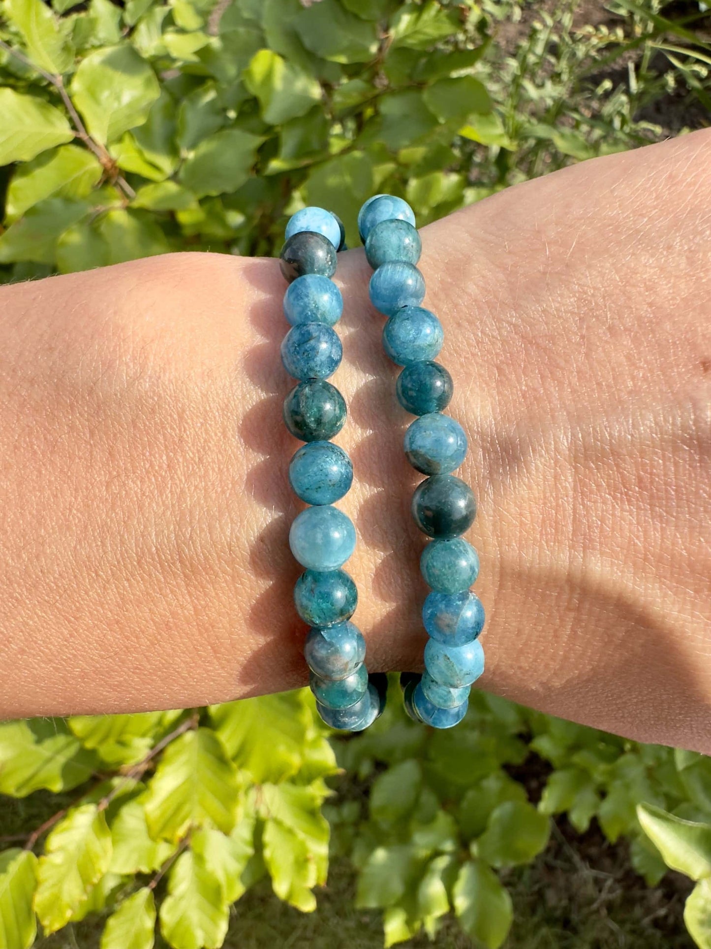 To armbånd af blå Apatit på en arm fotografet udendørs med grønne blade i baggrunden.