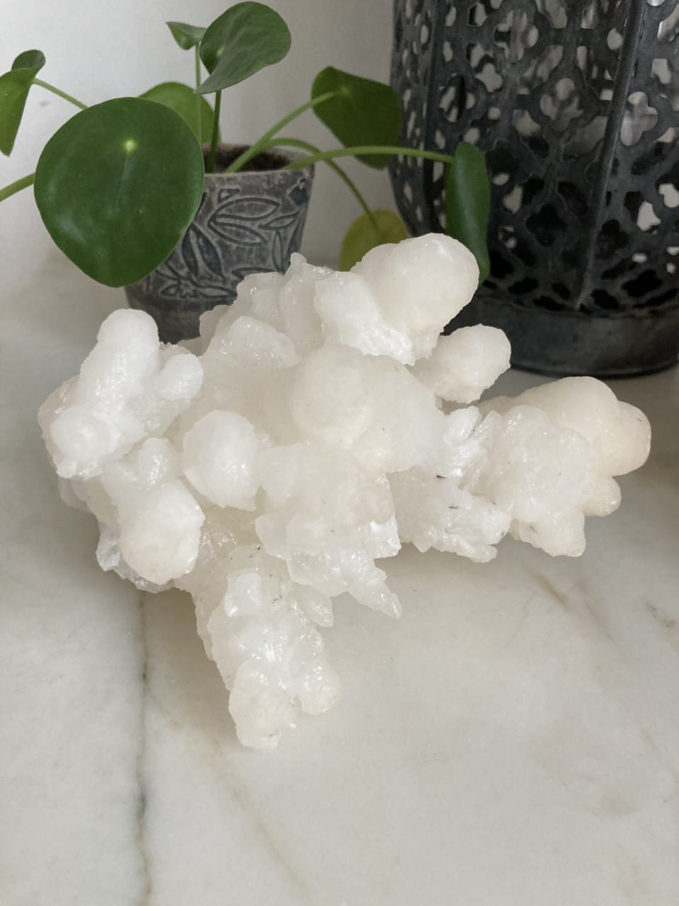 Calcit klynge på en marmorbord ved siden af en grøn plante i potte og en dekorativ lanterne.