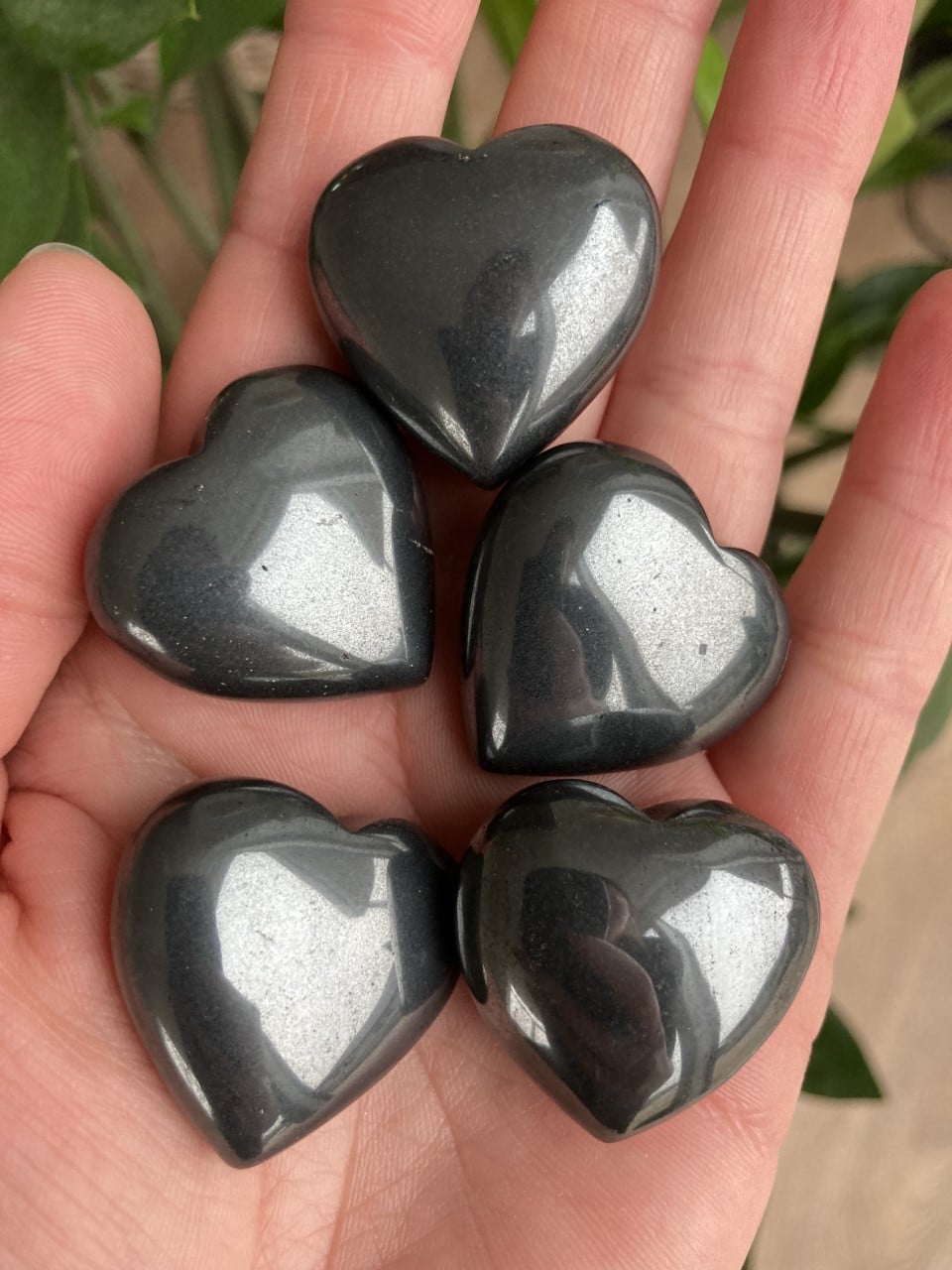 Hånden holder fem skinnende hæmatit hjerter mod en grøn baggrund.