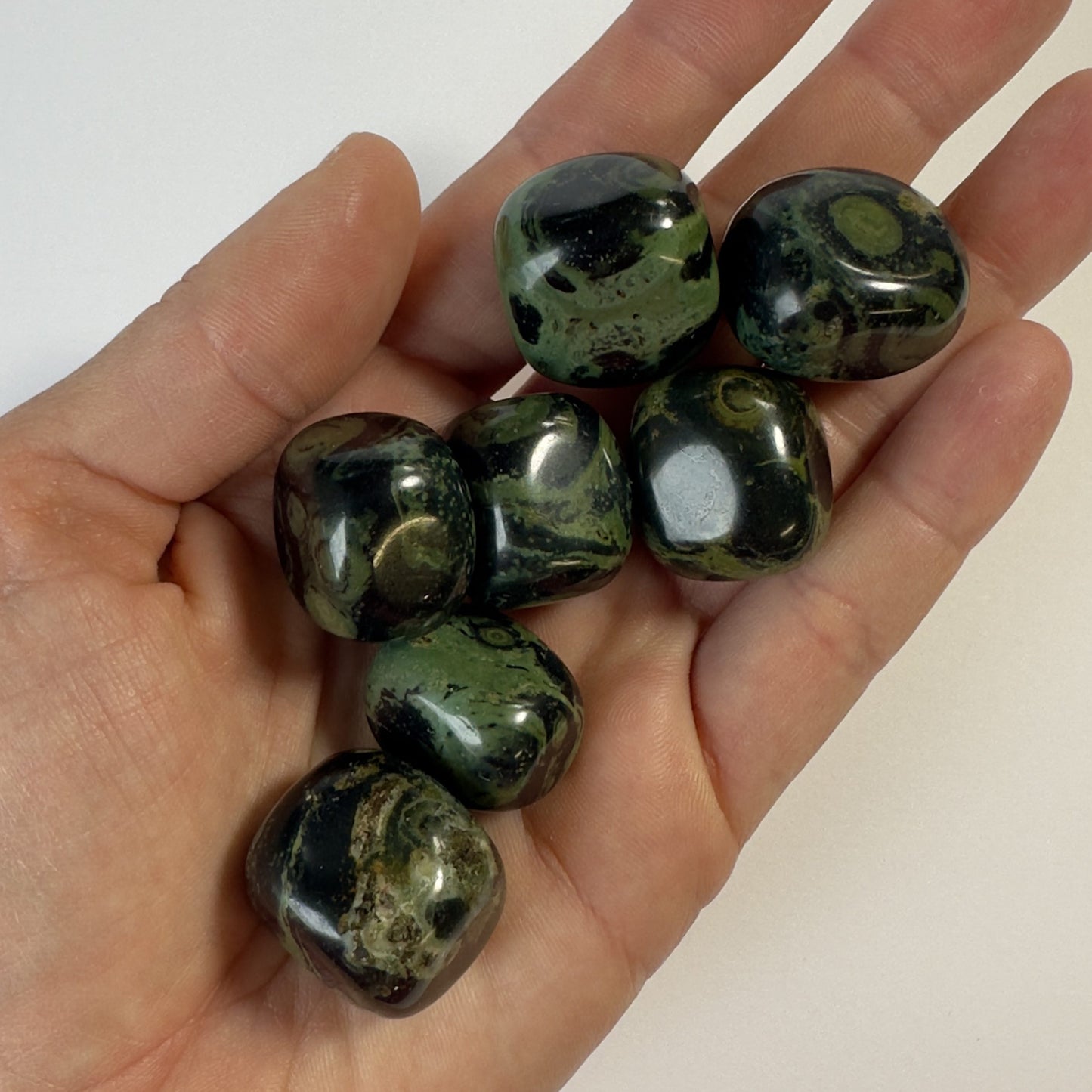 Hånd holder flere polerede Jaspis Kabamba lommesten.