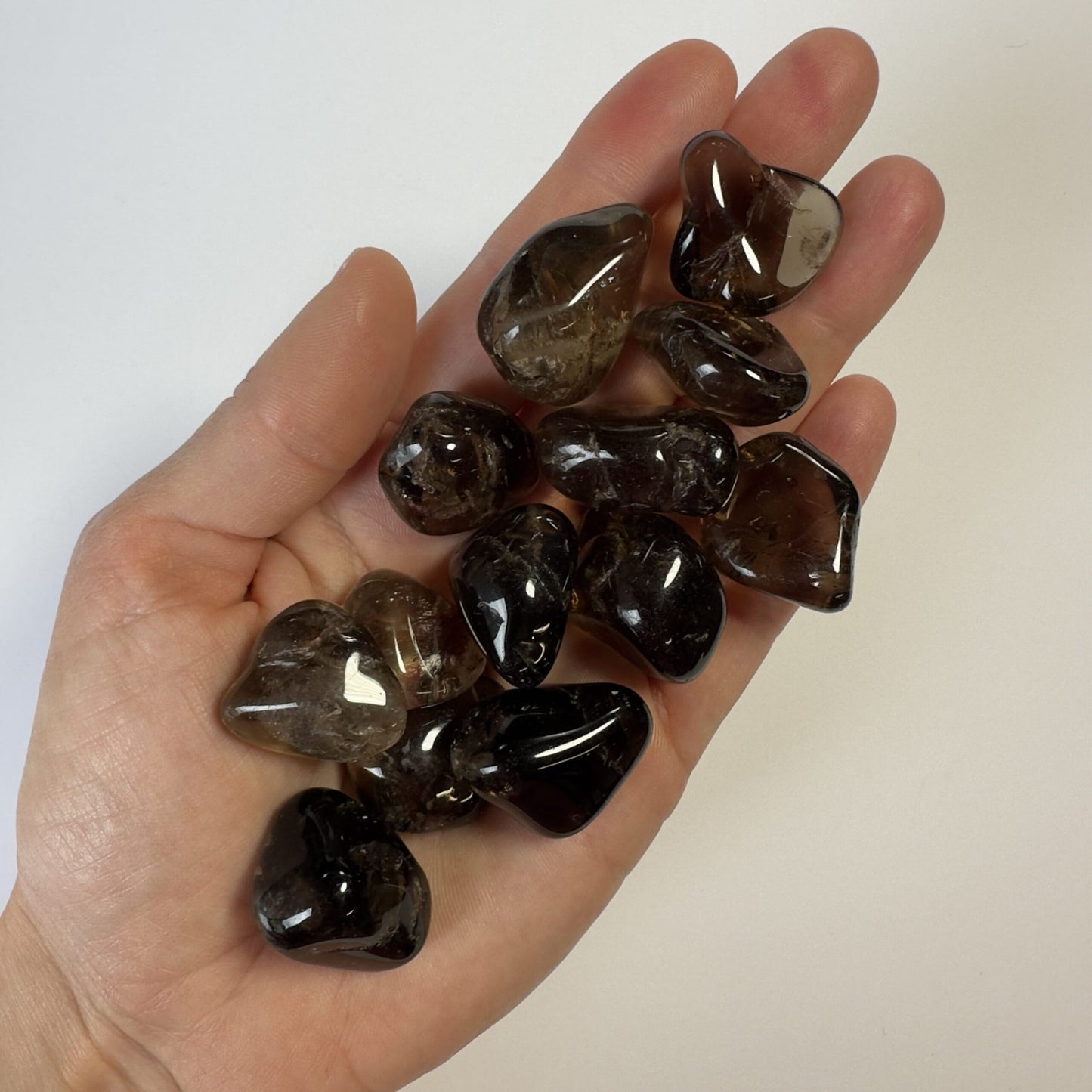 Hånd fuld af røgkvarts lommesten i forskellige nuancer, mod en hvid baggrund.