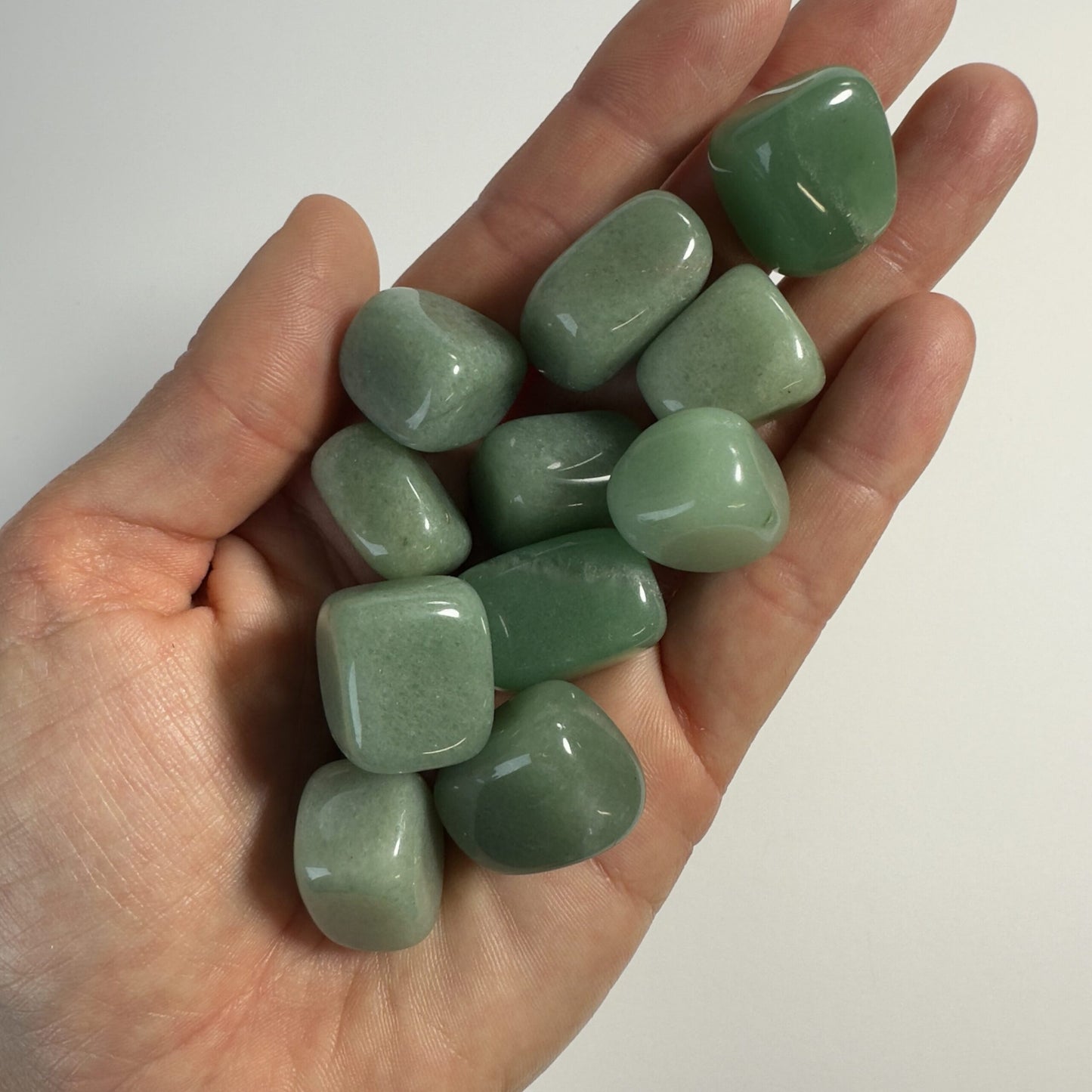 En håndfuld grøn aventurin lommesten i forskellige nuancer, liggende i en hånd.