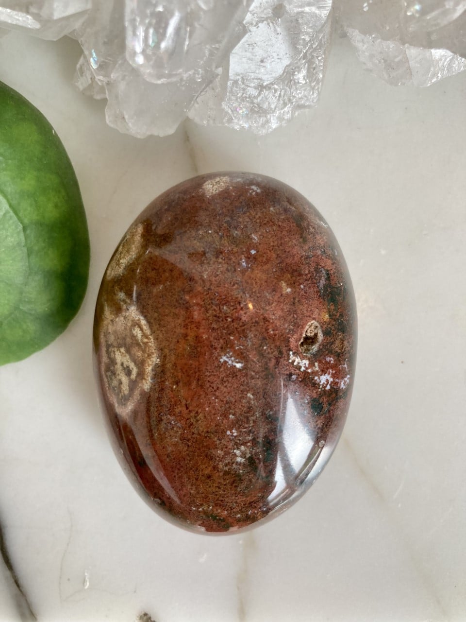 Jaspis Hav palmsten på lys overflade, omgivet af grønne blade og krystaller.