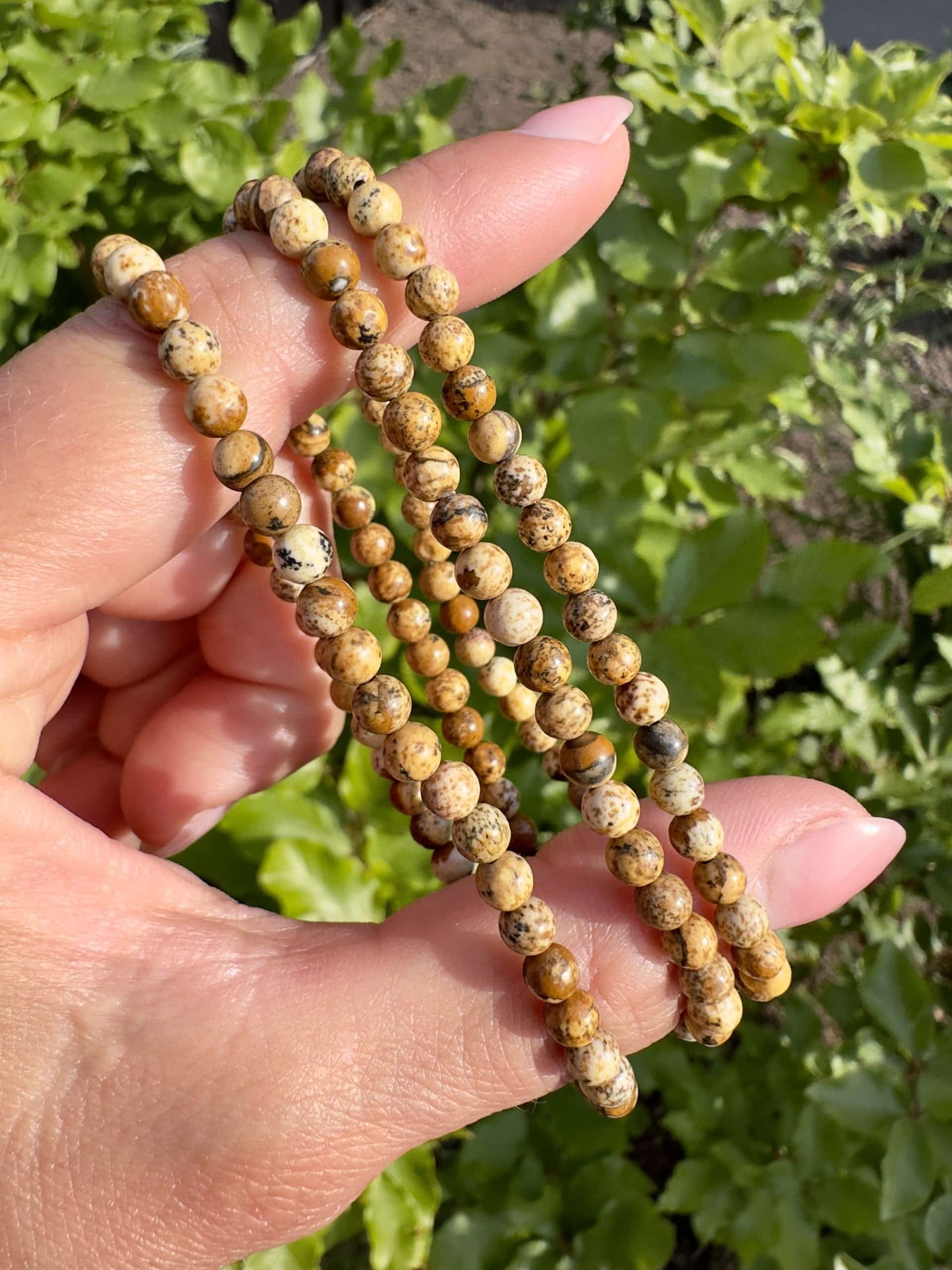 Hånd der holder tre Jaspis Landskabs armbånd op mod grøn baggrund.