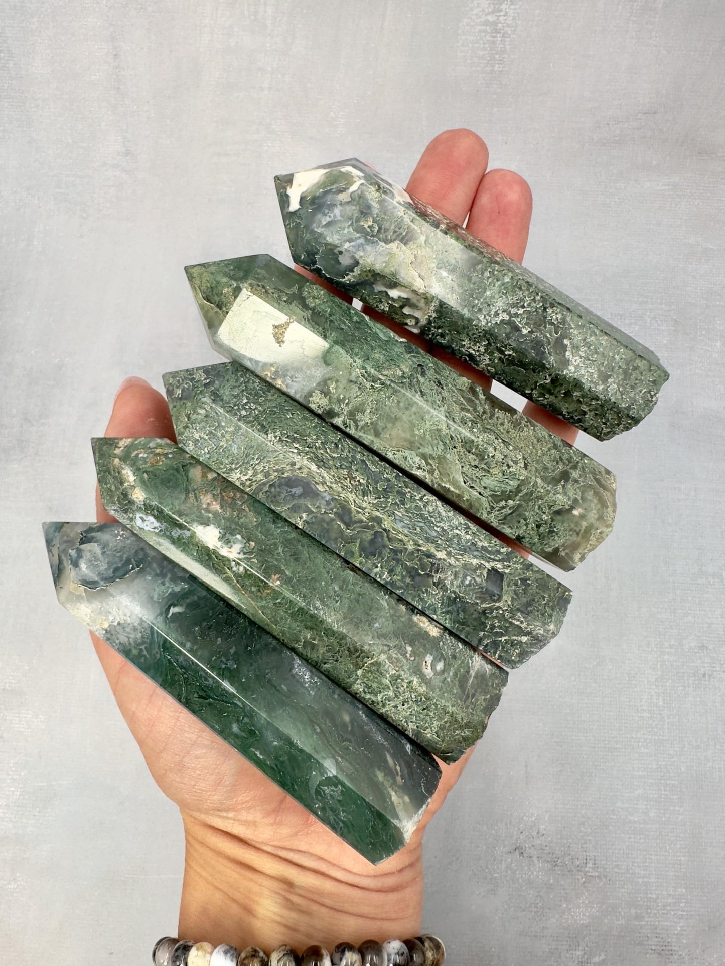 Hånd holder fem grønne Mos Agat tårne mod en grå baggrund.