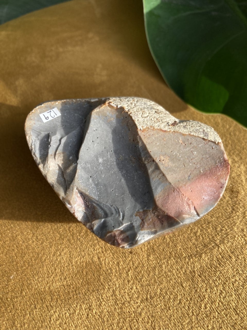 Hjerteformet Jaspis Polychrome-sten på brun baggrund med grønne blade i baggrunden.