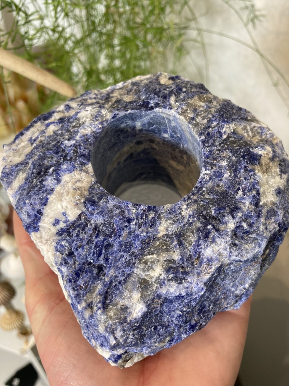 Sodalit fyrfadsstage nr 2, uregelmæssigt formet med blå og hvide nuancer, holdes i en hånd mod en grøn baggrund.