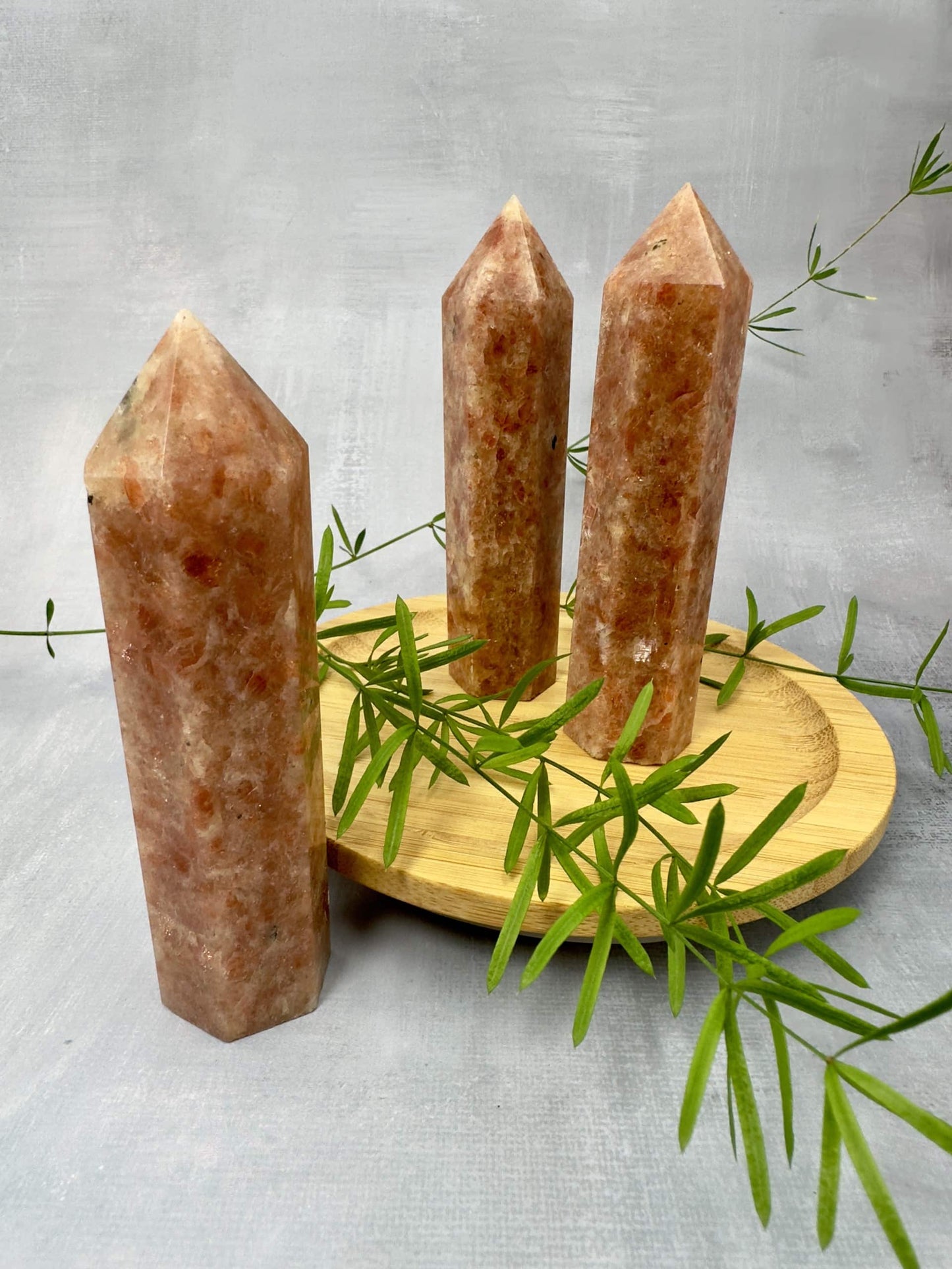 Tre solsten tårne på en træbakke med grønne grene i baggrunden.