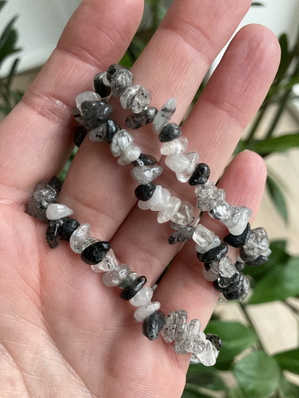 En hånd holder et turmalinkvarts armbånd med sorte og klare stenperler.