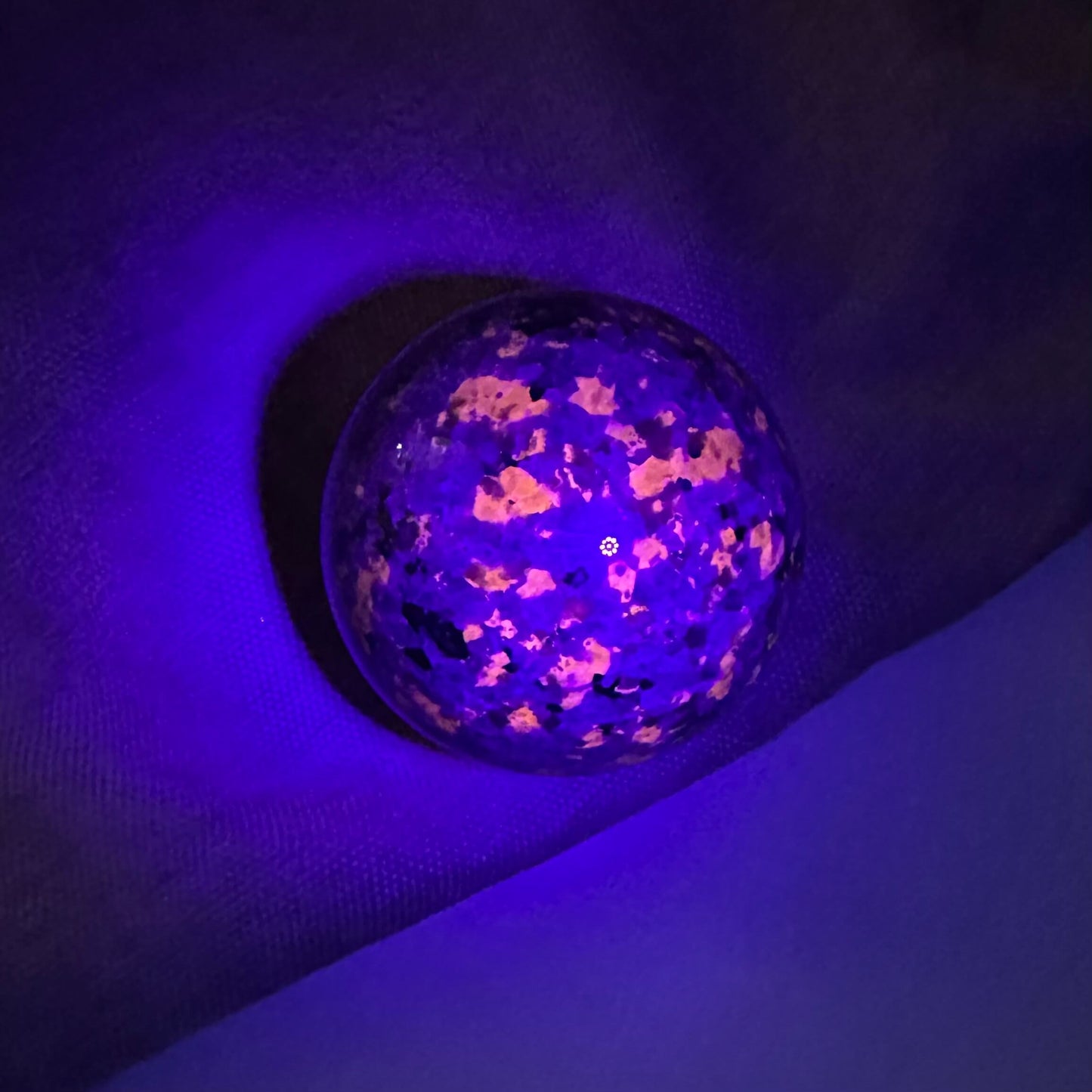 Yooperlit kugle under UV-lys, der afslører lysende mønstre på en mørk baggrund.