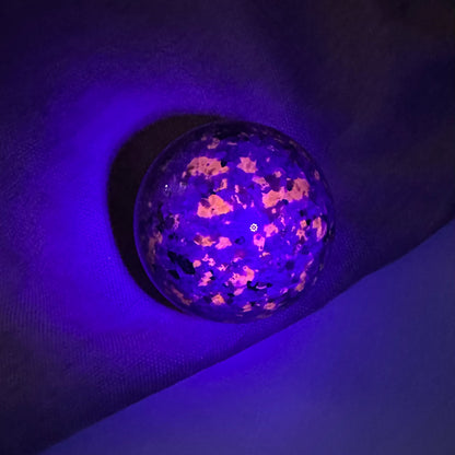 Yooperlit kugle under UV-lys, der afslører lysende mønstre på en mørk baggrund.