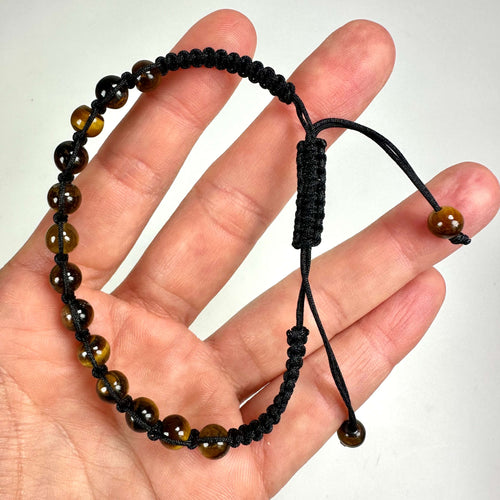 Hånd holder et Tigerøje armbånd med brune perler og sort snor.