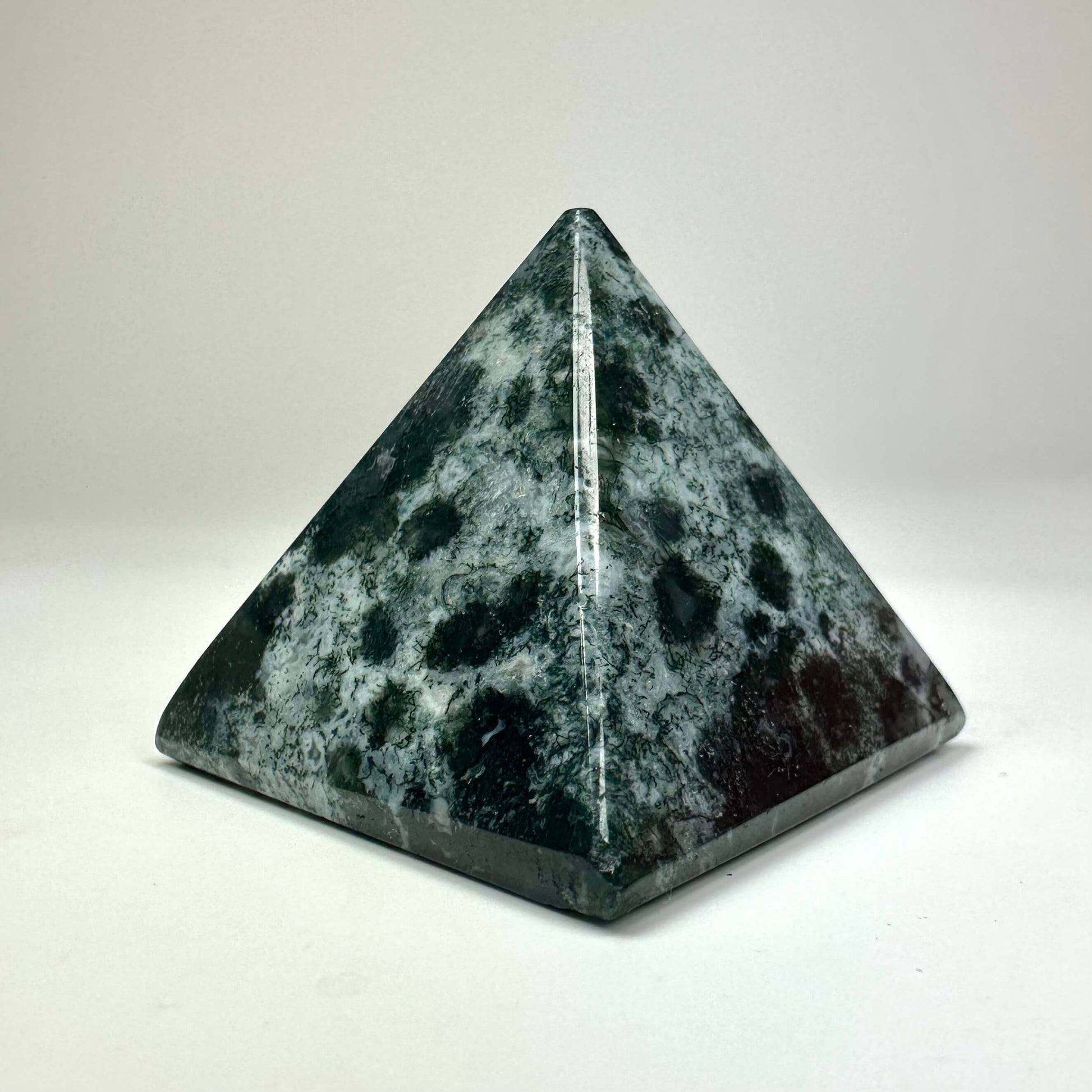 Grøn og sort pyramide lavet af natursten på en hvid baggrund.