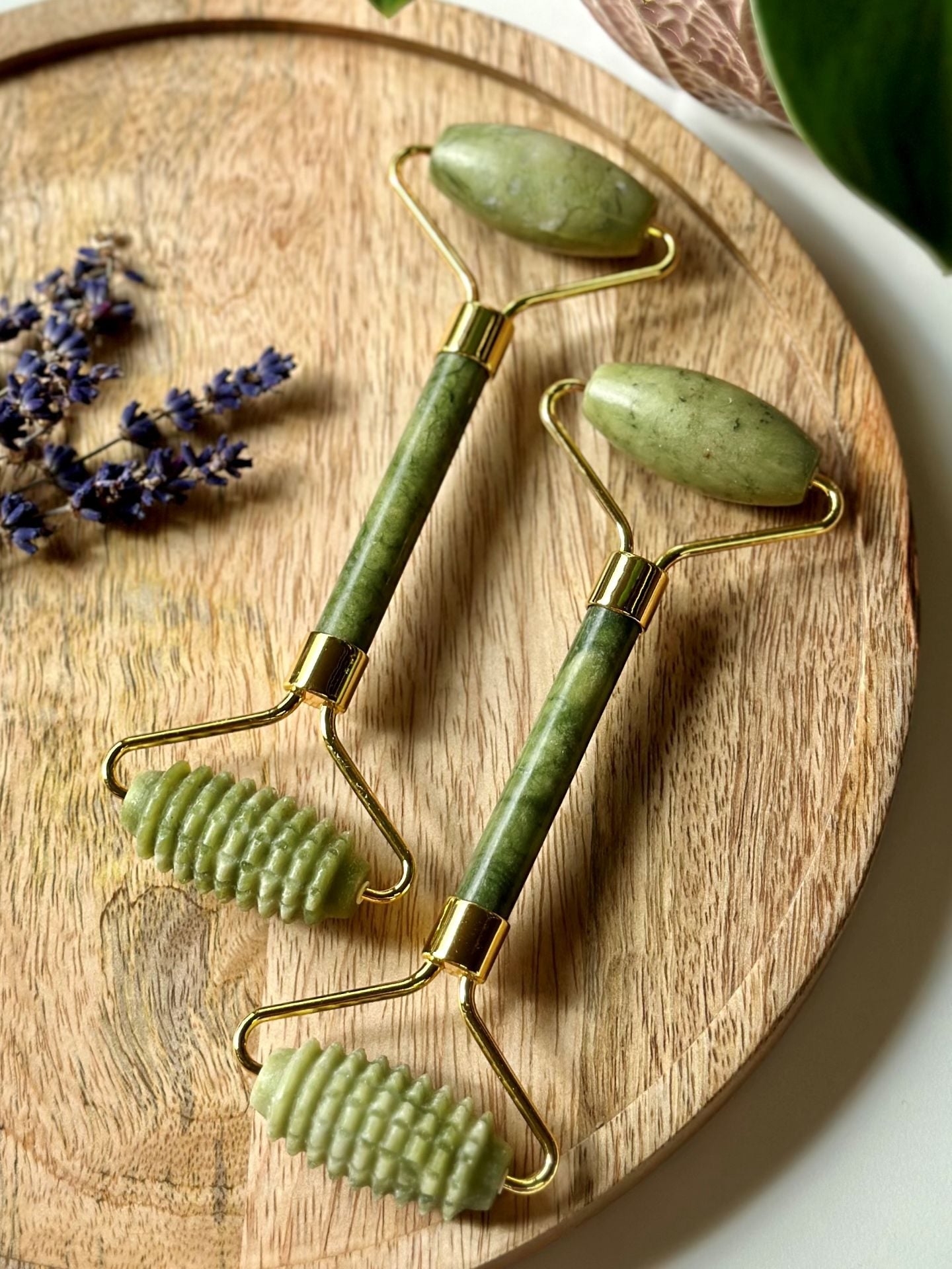 To grønne jade ansigtsruller på en træbakke ved siden af tørret lavendel.