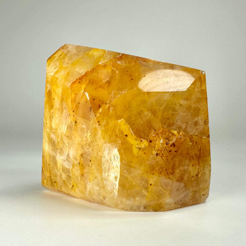 Golden healer krystal i fri form med gylden farve og naturlig tekstur mod neutral baggrund.