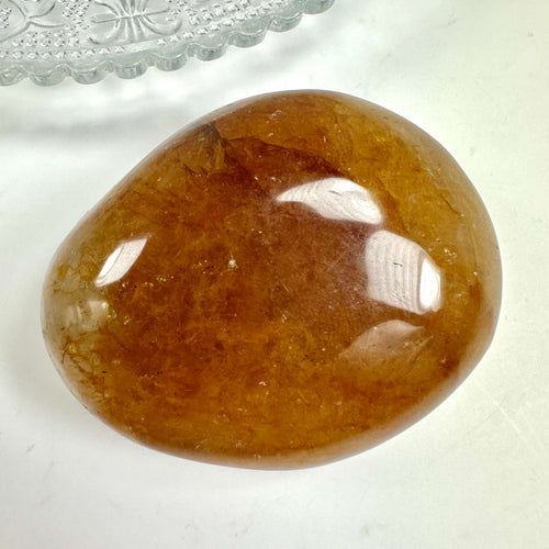 Golden healer håndsten med glat, gylden overflade, ligger på hvid baggrund ved siden af en dekorativ glasplade.