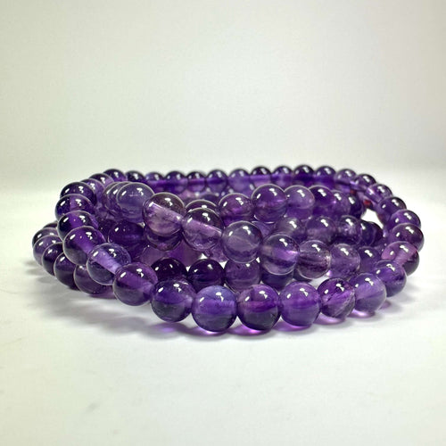 Armbånd med runde lilla ametystperler i tre rækker, lagt på en hvid overflade.