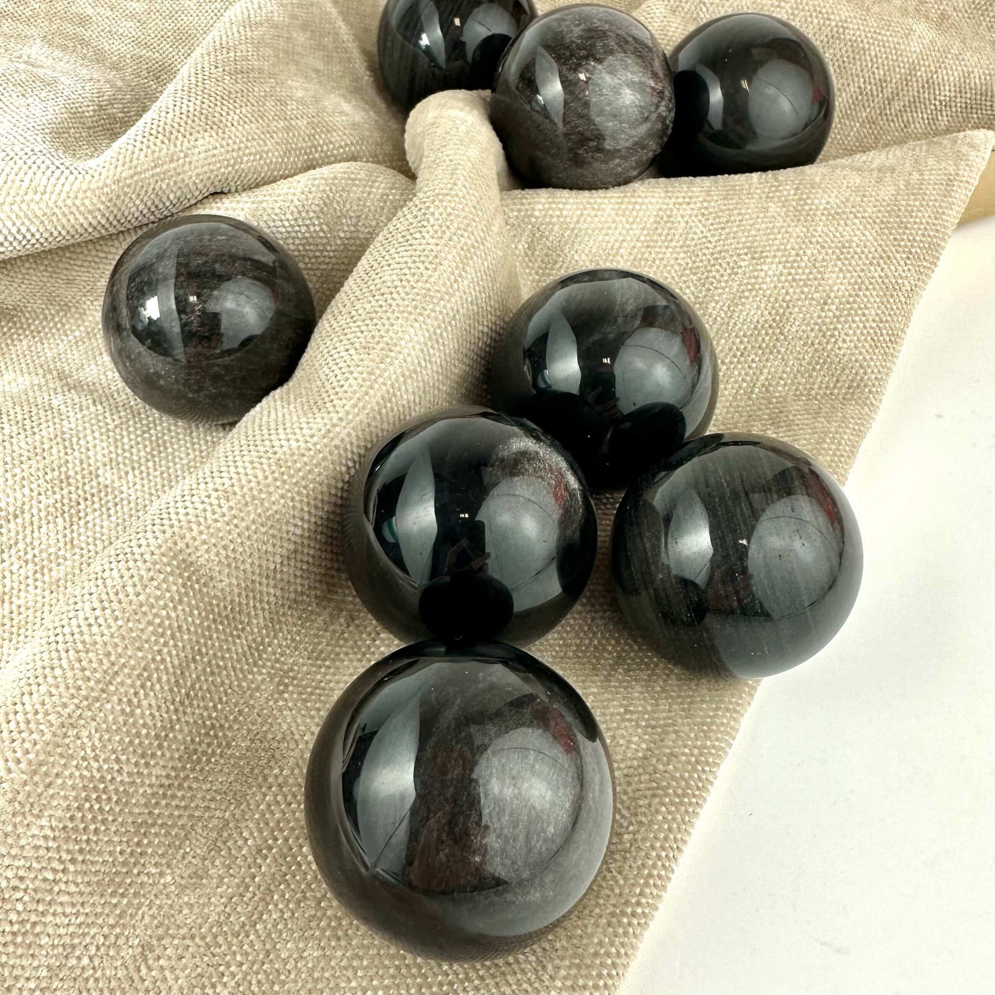 Obsidian gylden kugle i forskellige størrelser ligger på et beige tekstil underlag.