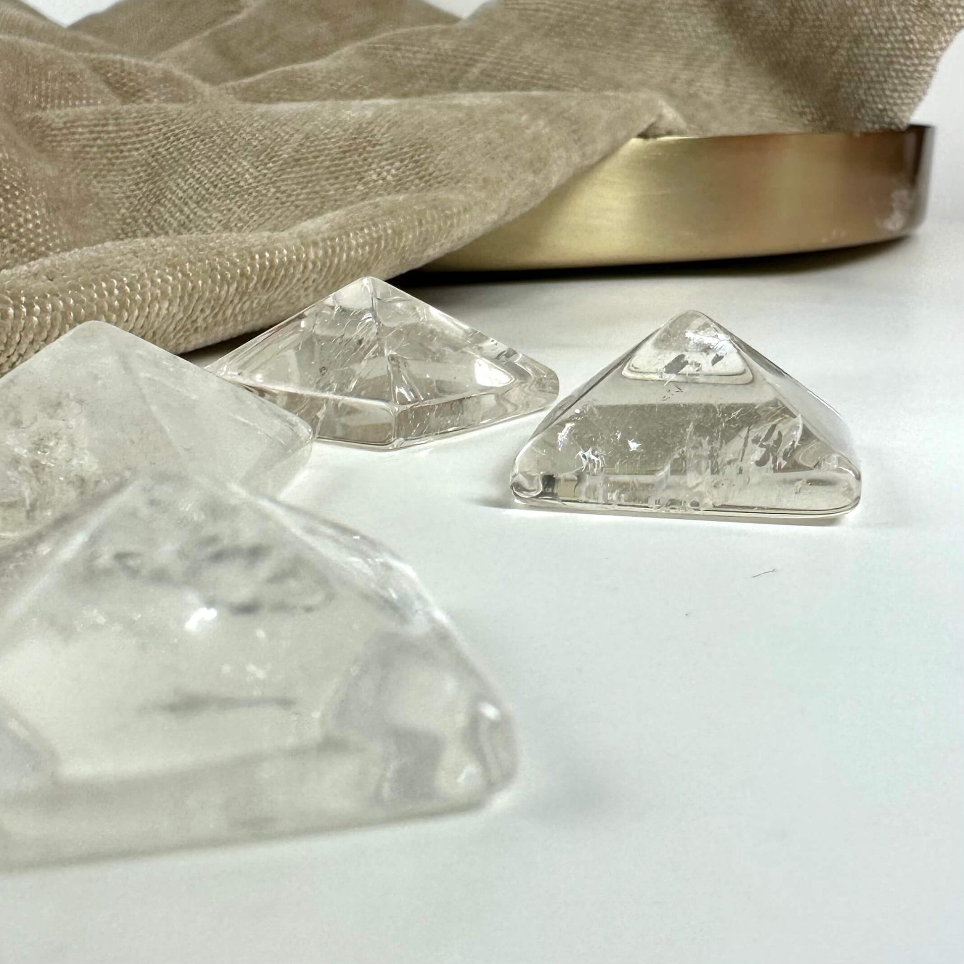 Bjergkrystal pyramider på en hvid overflade ved siden af en beige dug og guldfarvet bakke.