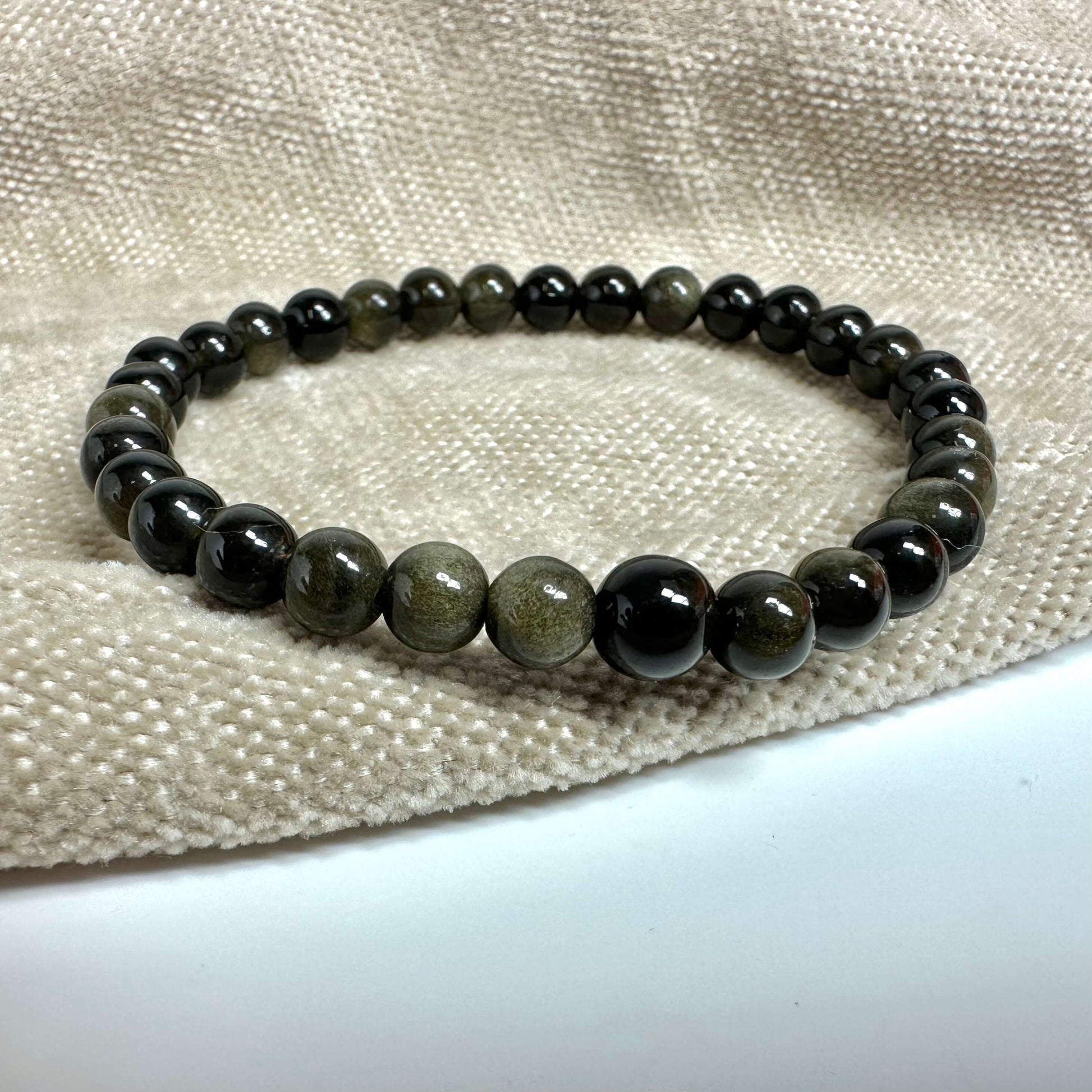 Armbånd opladningssæt inkl. gylden obsidian armbånd på en beige tekstilbaggrund.