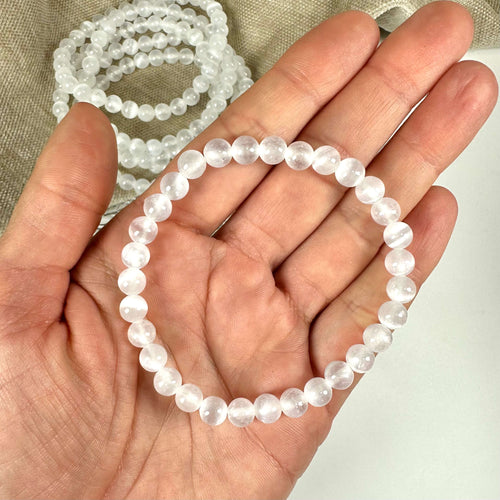 En person holder et selenit armbånd i hånden, med flere armbånd i baggrunden.