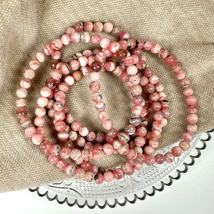 Lyserøde rhodochrosit perler på en glasplade med beige stofbaggrund.