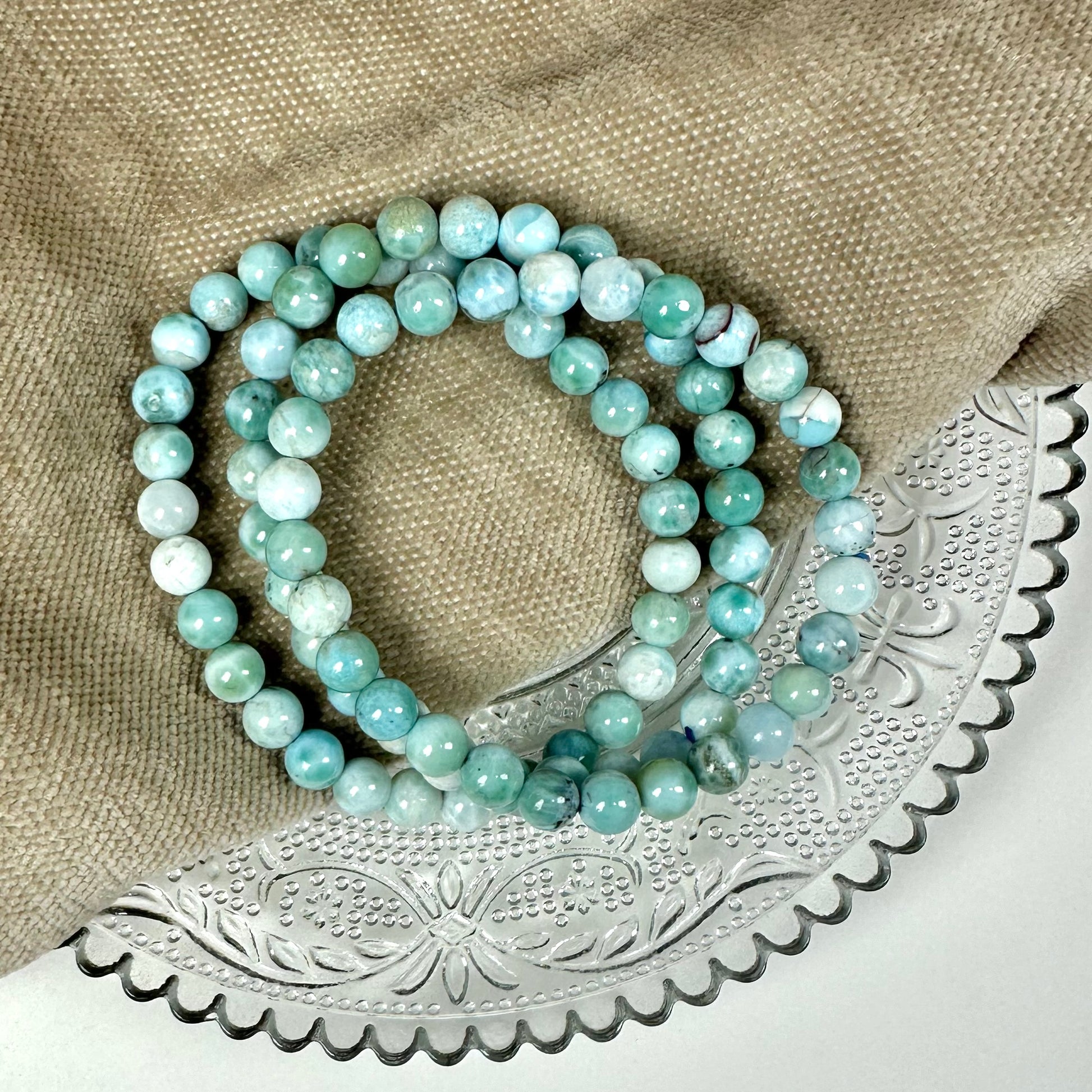 Larimar armbånd 6mm på en beige tekstiloverflade og en dekorativ metalbakke.