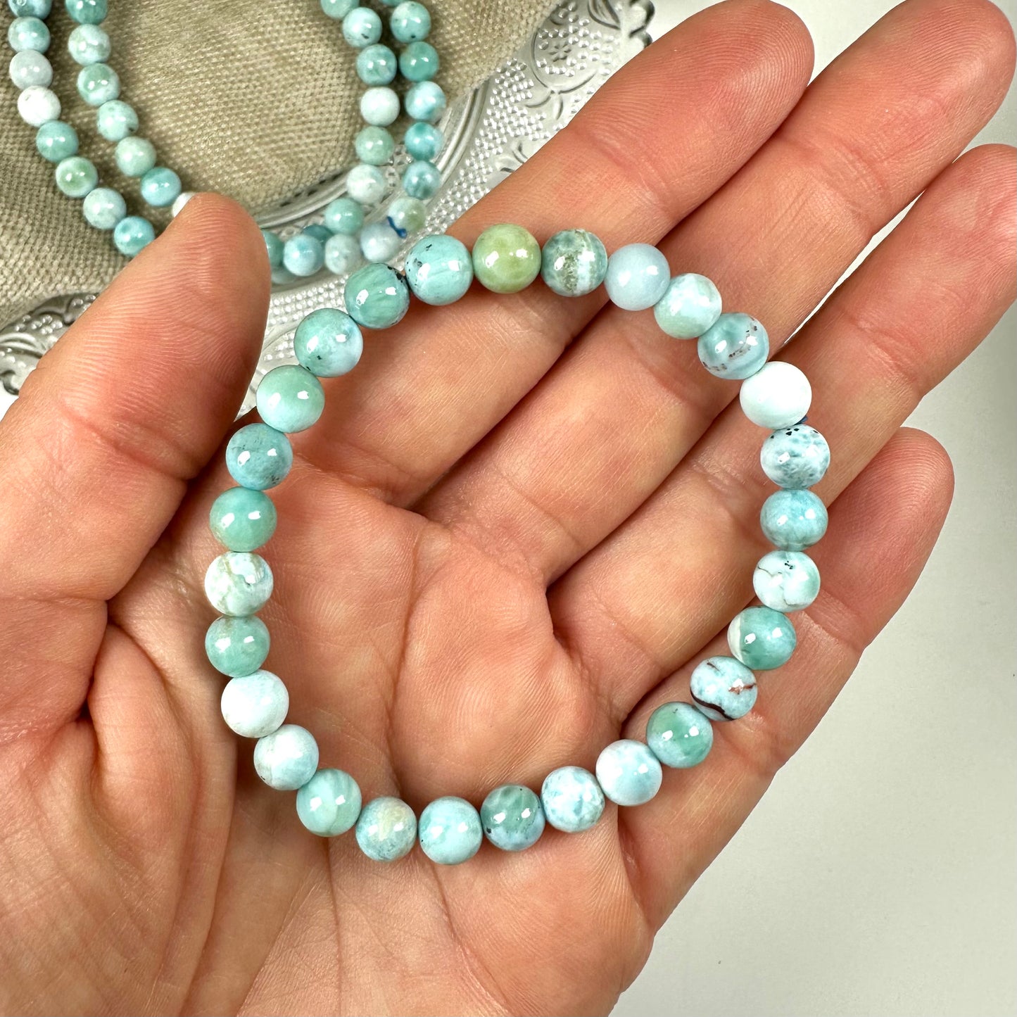 En hånd holder et 6mm Larimar armbånd med blå perler.