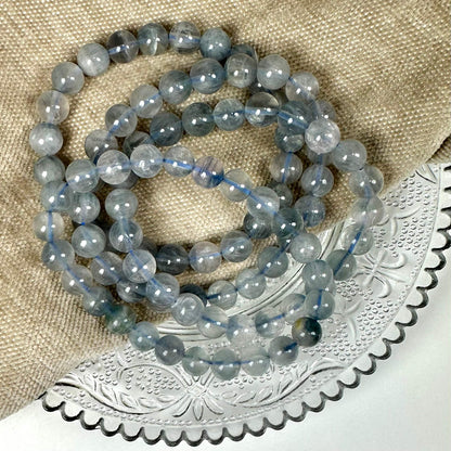 Blå fluorit armbånd 8mm ligger på en beige tekstil og dekoreret metalbakke.