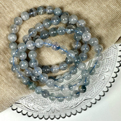 Blå fluorit armbånd 8mm ligger på en beige tekstil og dekoreret metalbakke.