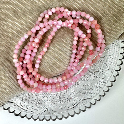 Pink opal armbånd 4mm facet vises på en detaljeret, rund bakke og beige tekstilbaggrund.