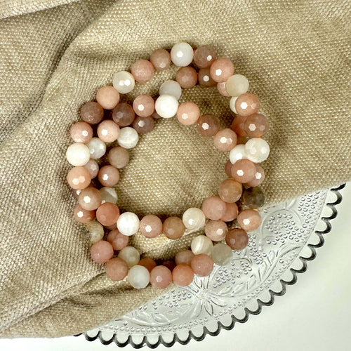 Månesten mix armbånd på beige stof og dekorativt glasfad.