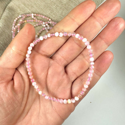 En hånd holder et Blomster Agat armbånd med små, lyserøde perler mod en neutral baggrund.