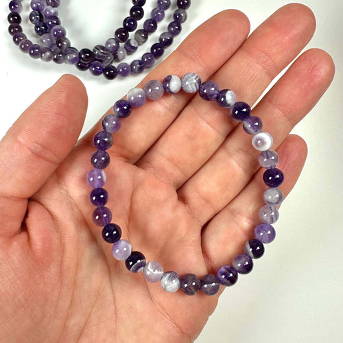 Hånd holder et Ametyst Chevron armbånd 6mm med lilla perler, set mod en hvid baggrund.