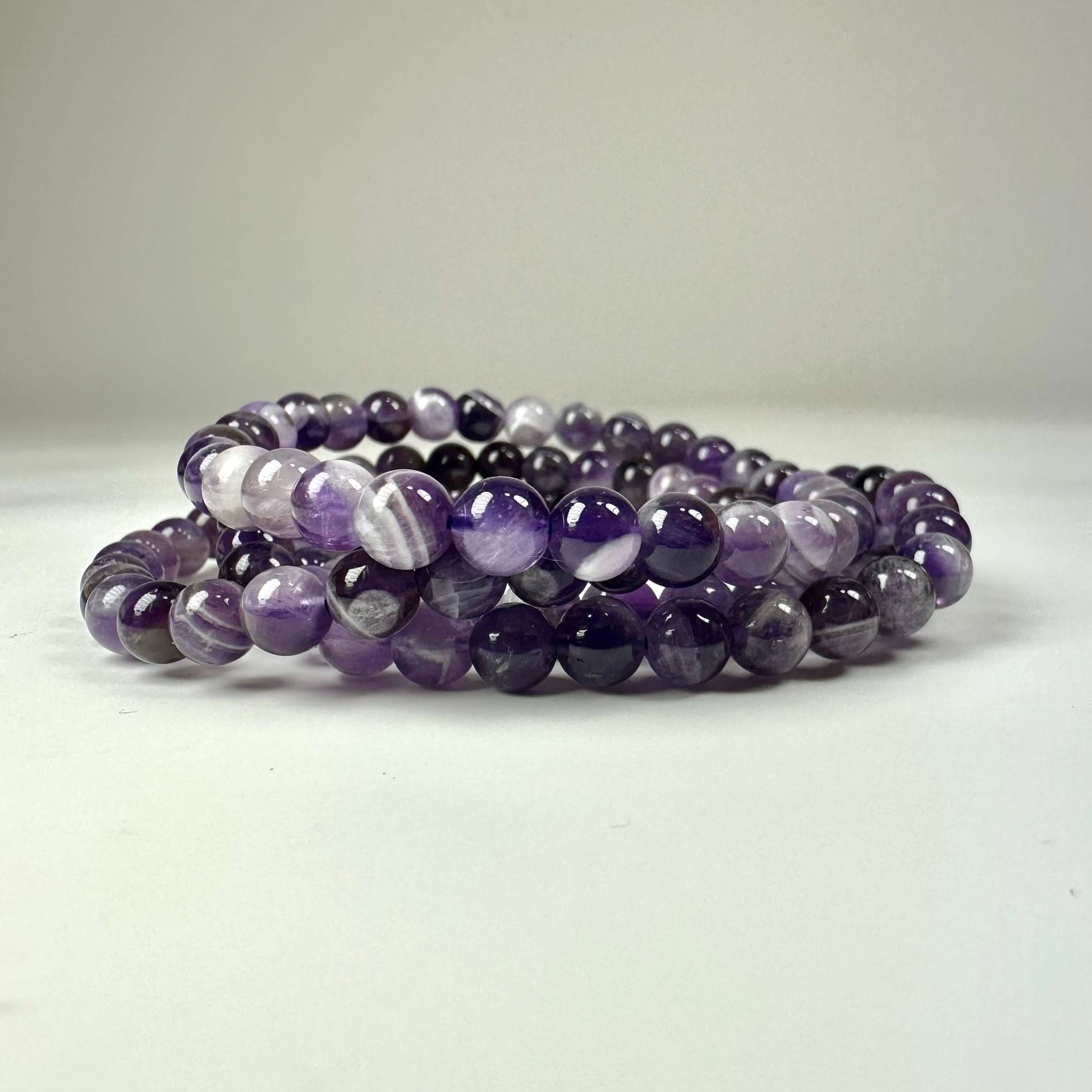Ametyst Chevron armbånd 6mm med perler i nuancer af lilla og hvid, elegant placeret på en lys baggrund.