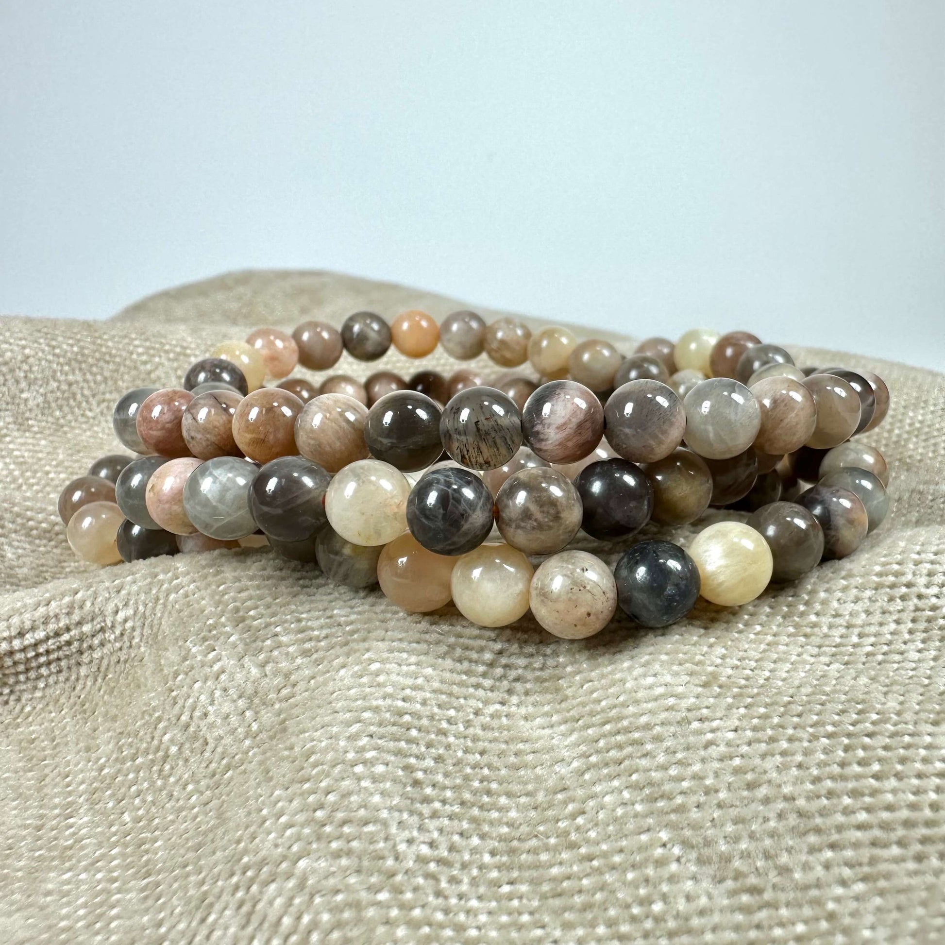 En stabel farverige stenkuglearmbånd ligger på en beige klud.