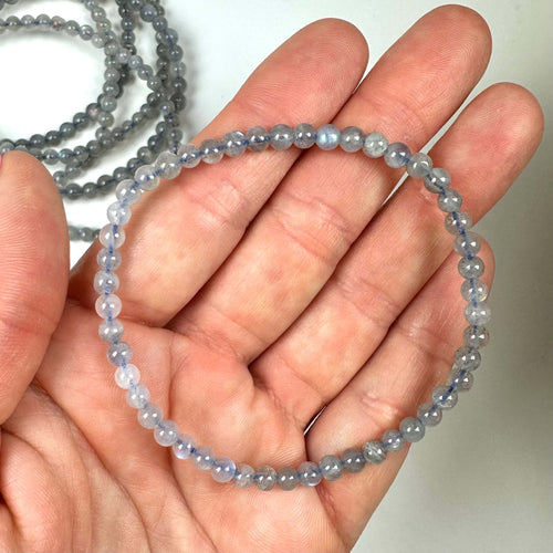 Person holder et Labradorit armbånd lavet af små, skinnende perler i hånden.