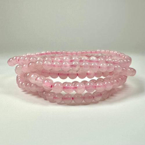 Kugler af rosa kvarts perler stablet i en spiralform på en hvid baggrund.