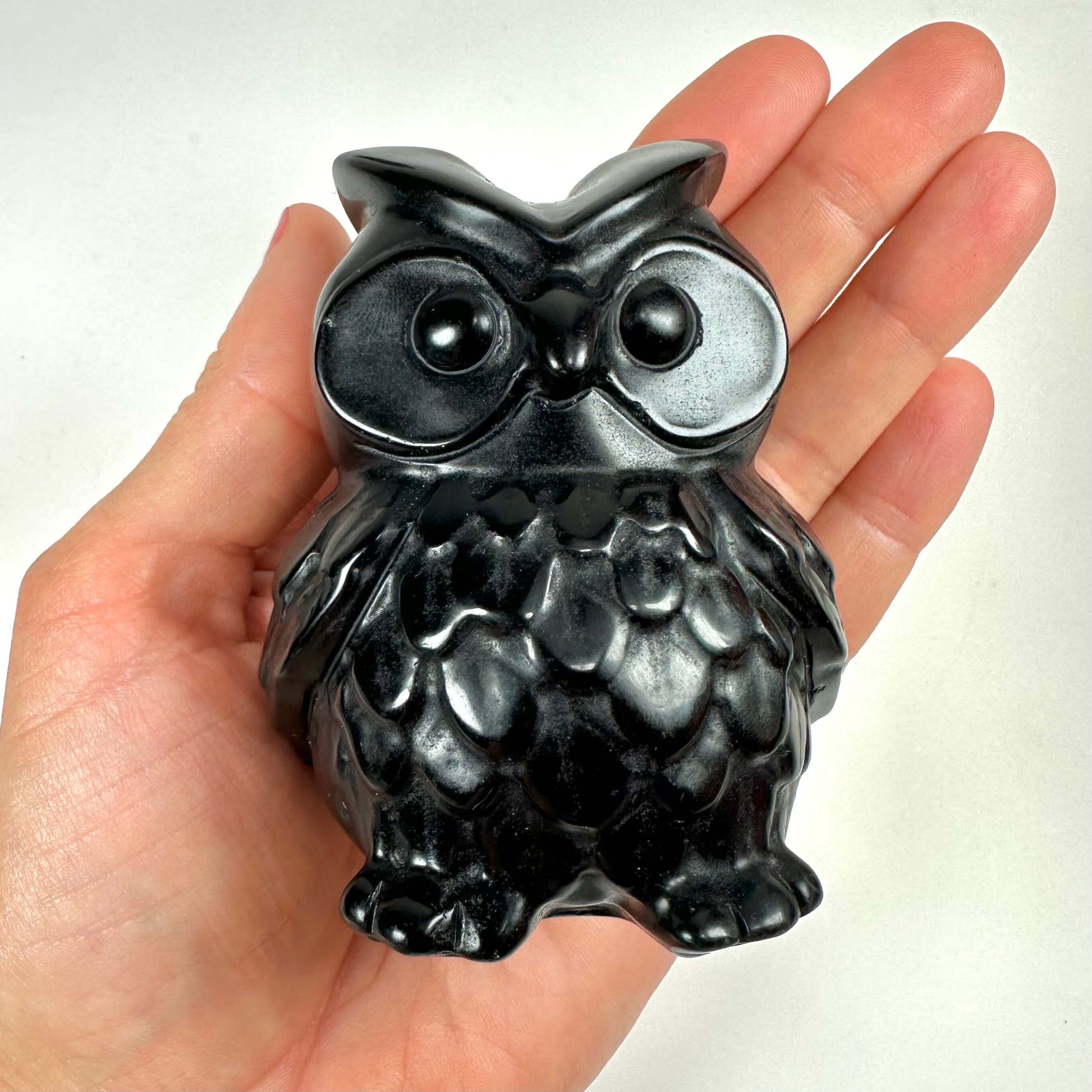 En hånd holder en sort obsidian ugle med detaljerede fjer og store øjne.