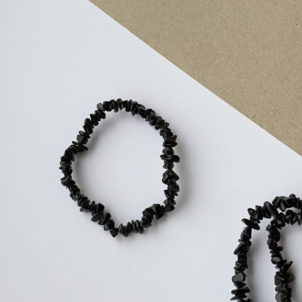 Obsidian sort armbånd med ujævne perler på en hvid og beige baggrund.