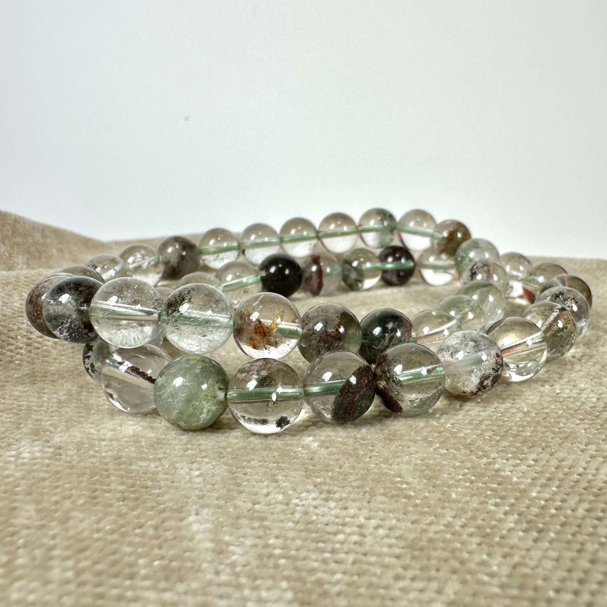 En gennemsigtig krystalarmbånd med farvede indlejringer ligger på en beige overflade.