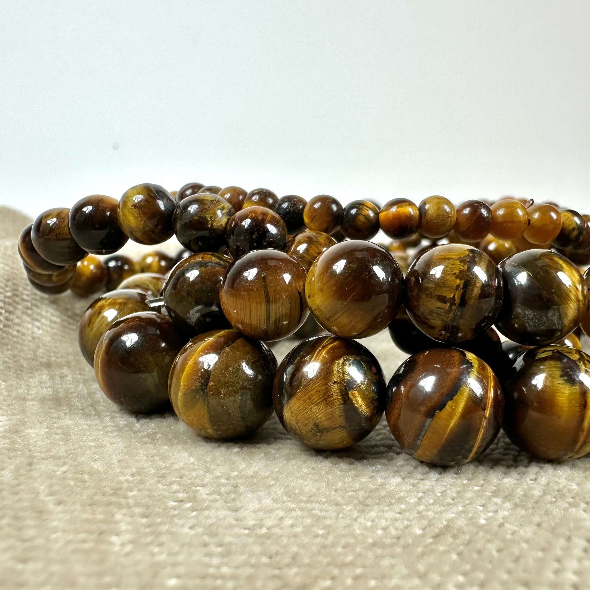Tigerøje-perler i forskellige størrelser på en lys beige overflade. Skinnende overflade med brune og gyldne nuancer.