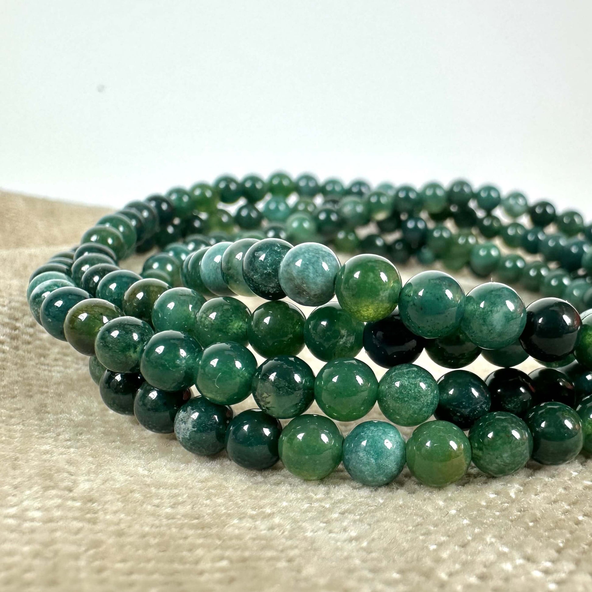 Grønne perlearmbånd i flere rækker på en beige overflade.