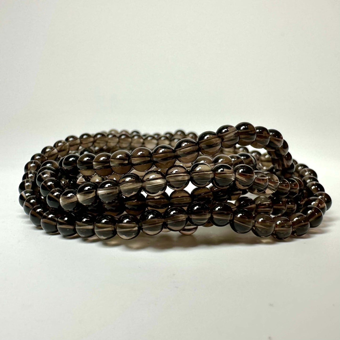 Et tæt bånd af røgkvartsperler i mørkebrun farve på en hvid baggrund.