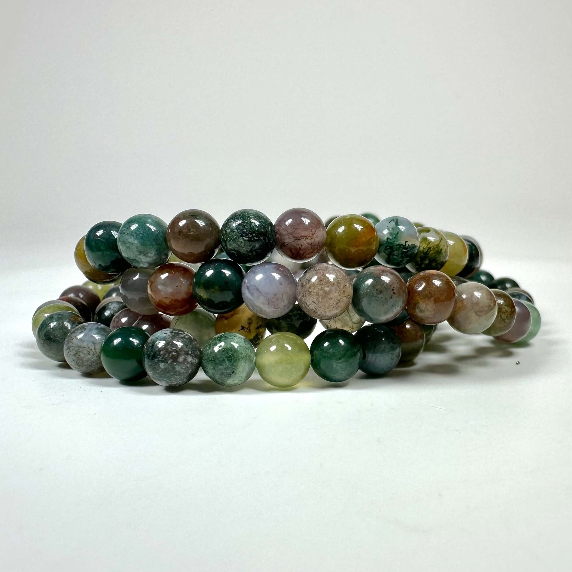 Armbånd med flerfarvede perler i grønne, brune og grå nuancer på en hvid baggrund.