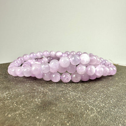 Et armbånd af lyserøde perler ligger på en tekstureret overflade.