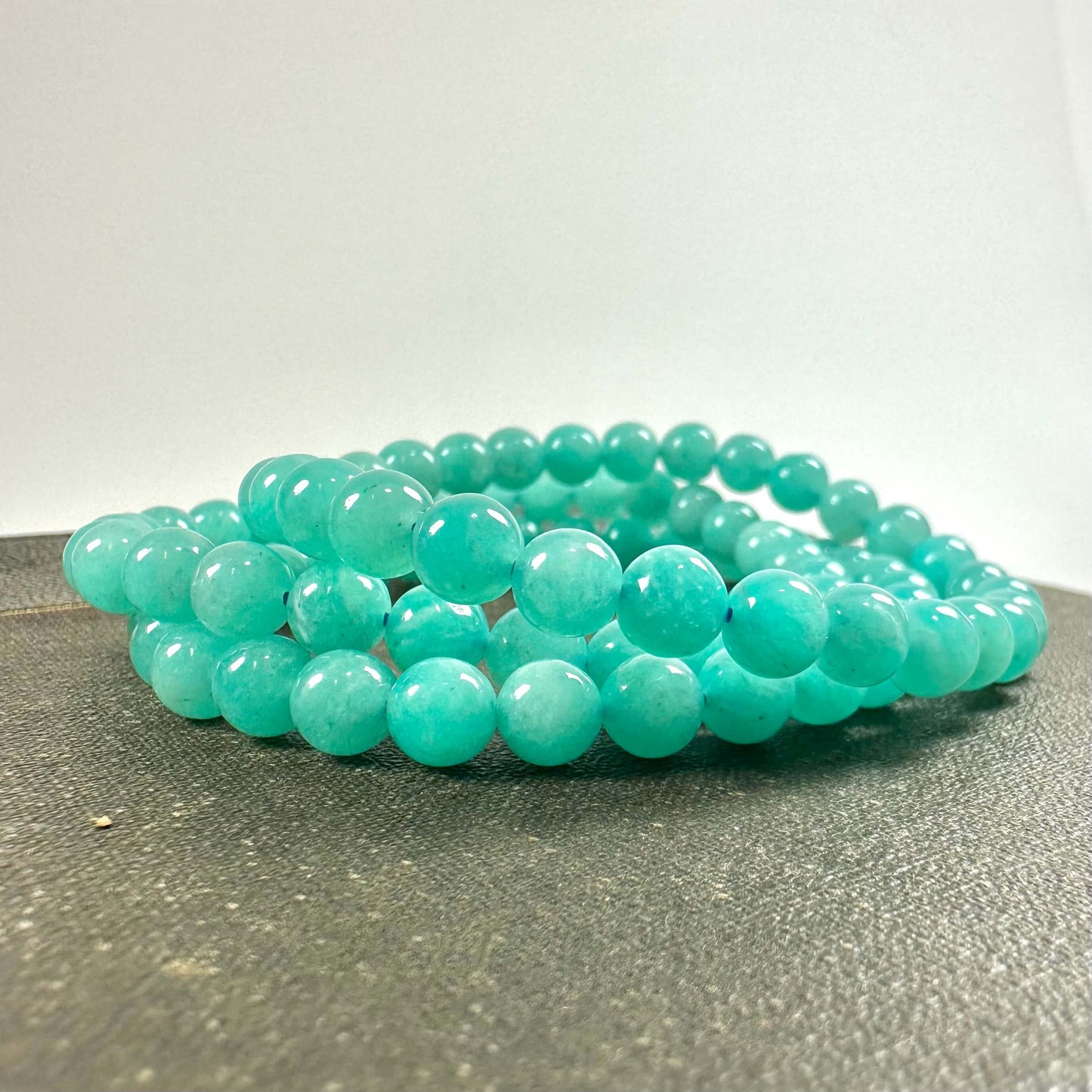 Turkis perlekæde lagt på en grå overflade med en enkel hvid baggrund.